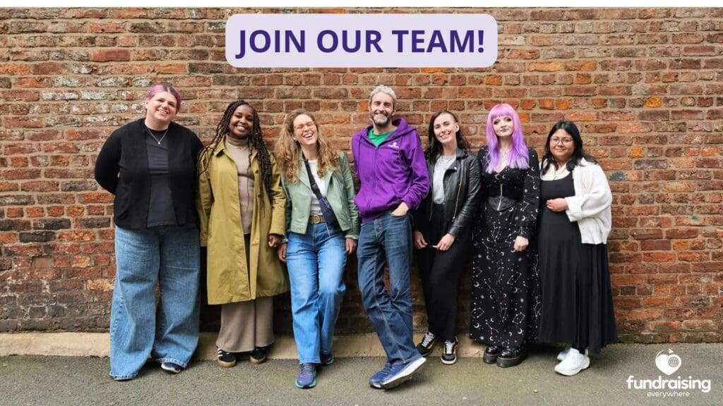 The fundraising everywhere team stand against a brick wall. From left to right: Meghan, a white woman with pink hair, she's wearing a black jacket and blue jeans. Cam, a black woman with long, dark hair. She wears a long camel coat and beige trousers. Alex, a white woman with light curly hair tied back. She wears a green jacket and blue jeans. Simon, a white man with short grey hair wears a purple hoody and dark jeans. Nikki, white woman with short dark hair. She wears a grey t shirt and black trousers. Jade, a white woman with long purple hair. She wears a black dress. Nori, an asian woman with short dark hair, she wears a black dress and white cardigan.